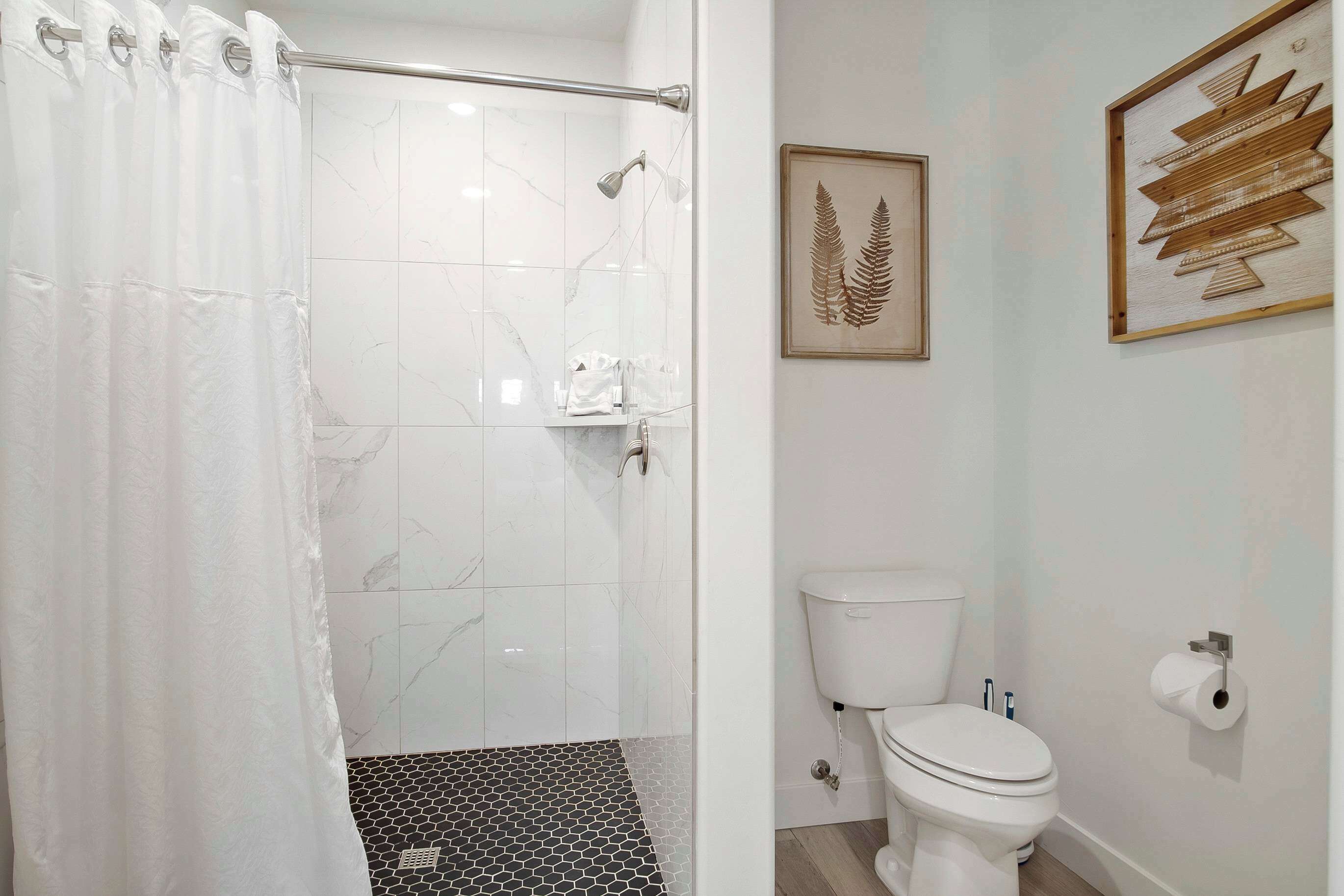 Une salle de bain avec une douche, des toilettes et une œuvre d’art encadrée au mur.