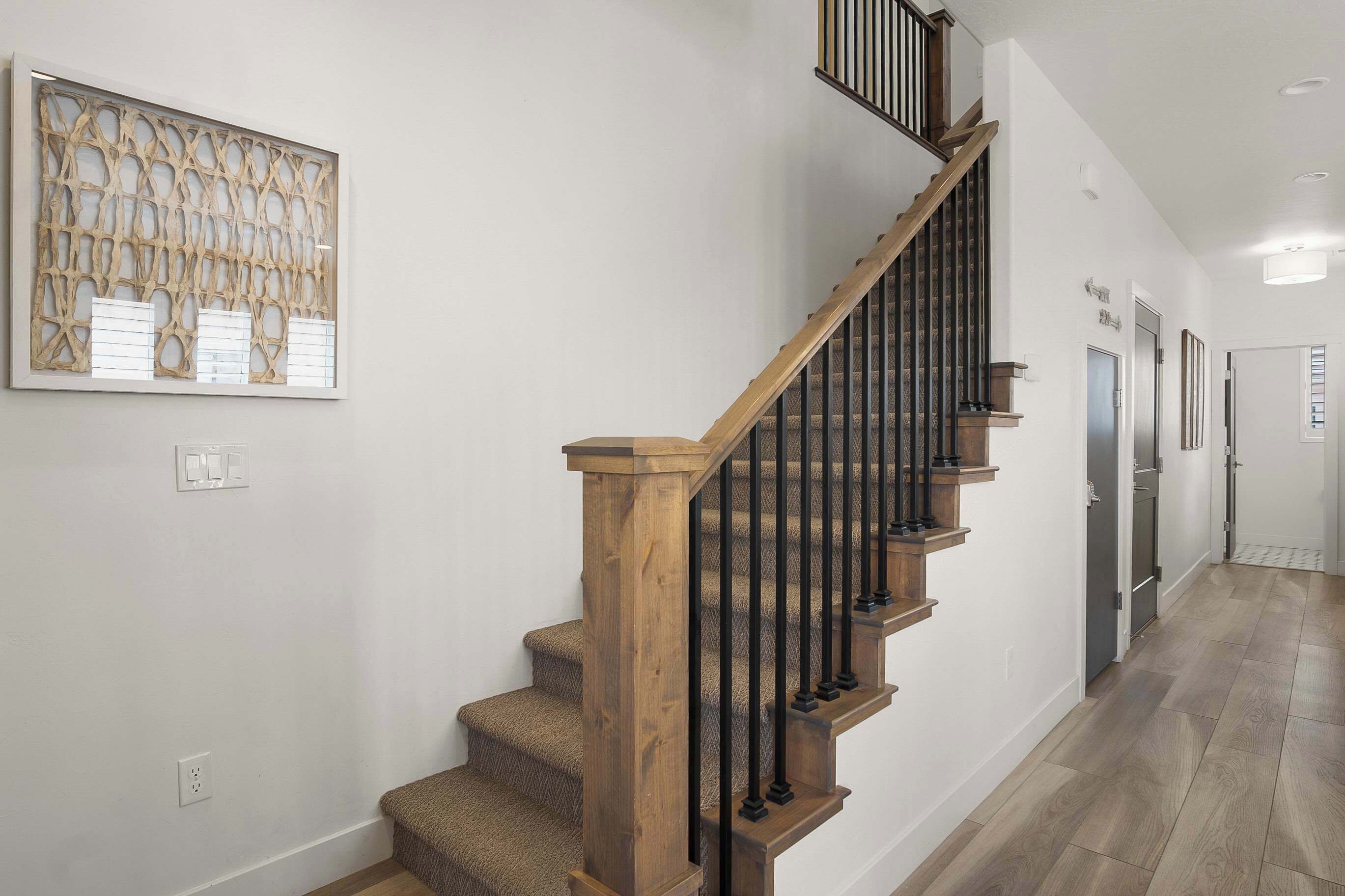A staircase with wooden steps and black railings, a wall-mounted artwork, and a hallway with a light-colored floor.