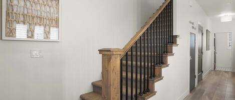 A staircase with wooden steps and black railings, a wall-mounted artwork, and a hallway with a light-colored floor.
