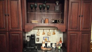 Una cocina con armarios de madera oscura, una cafetera, un hervidor de agua y diferentes tazas y vasos.