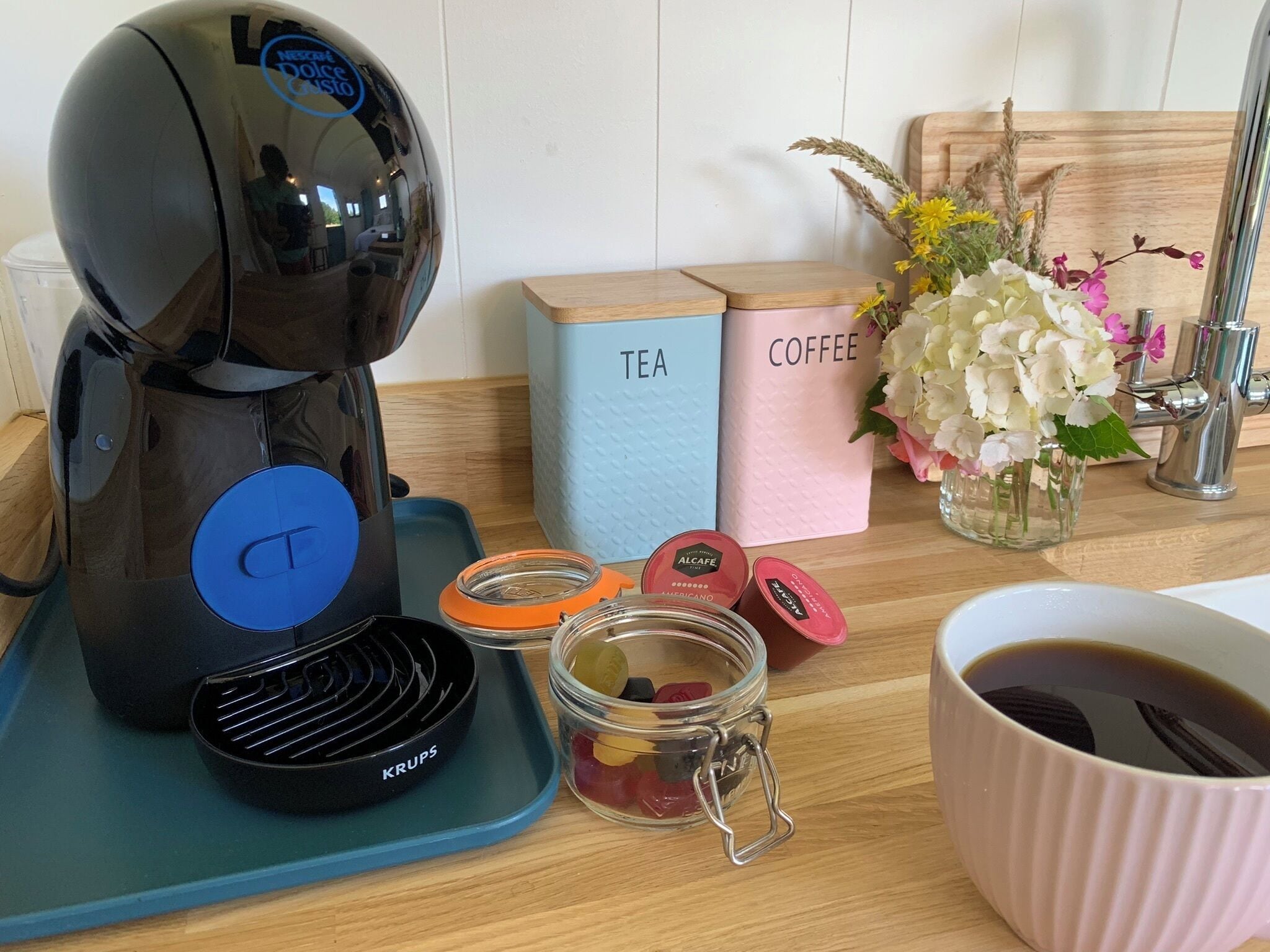 Une machine à café sur un plateau bleu, un bocal de bonbons, une tasse de café et des récipients étiquetés « THÉ » et « CAFÉ ».