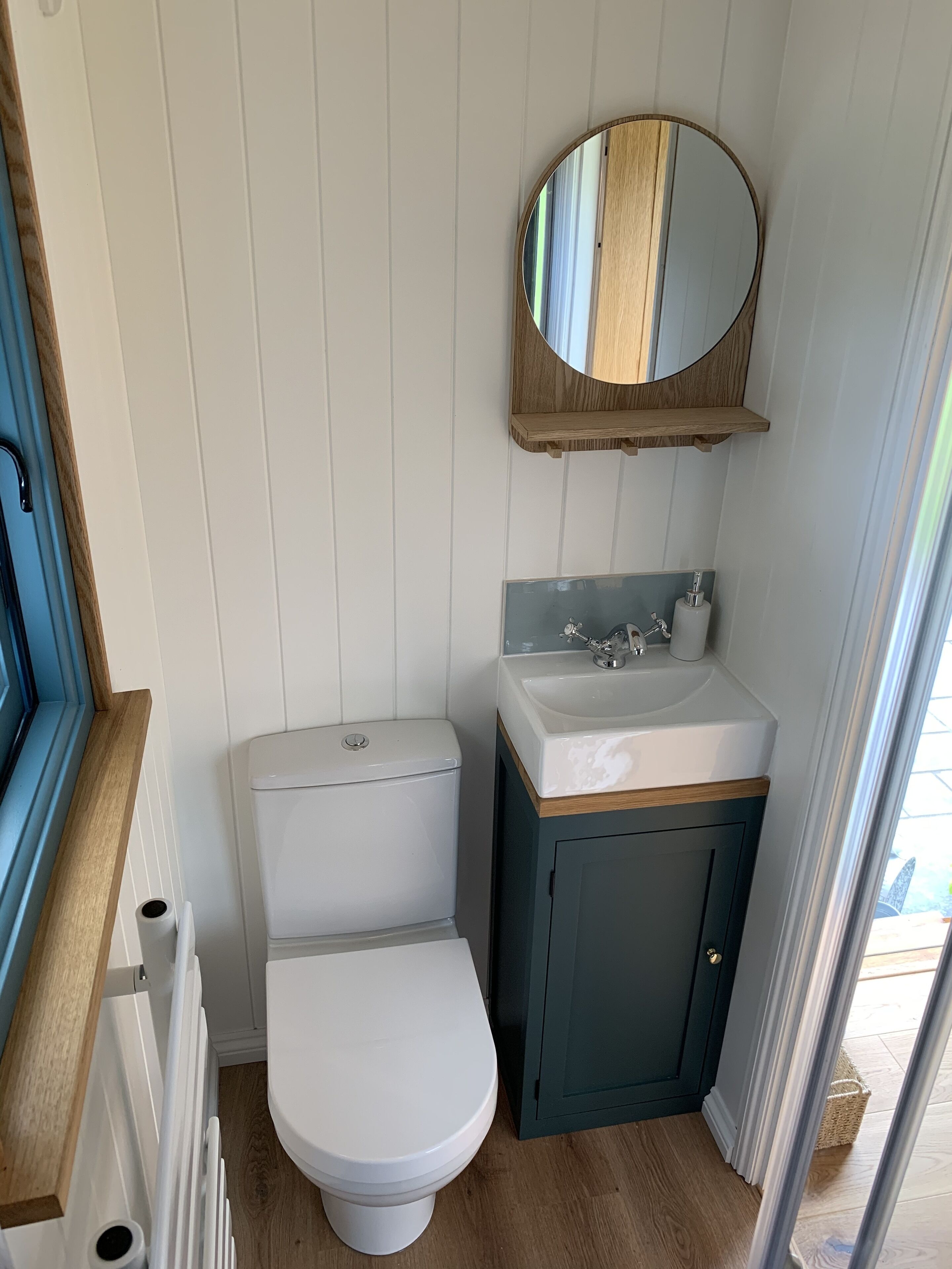 Ein kleines Badezimmer mit Toilette in Weiß, einem Spiegel mit Holzrahmen und einem weißen Waschbecken mit Holzauskleidung.