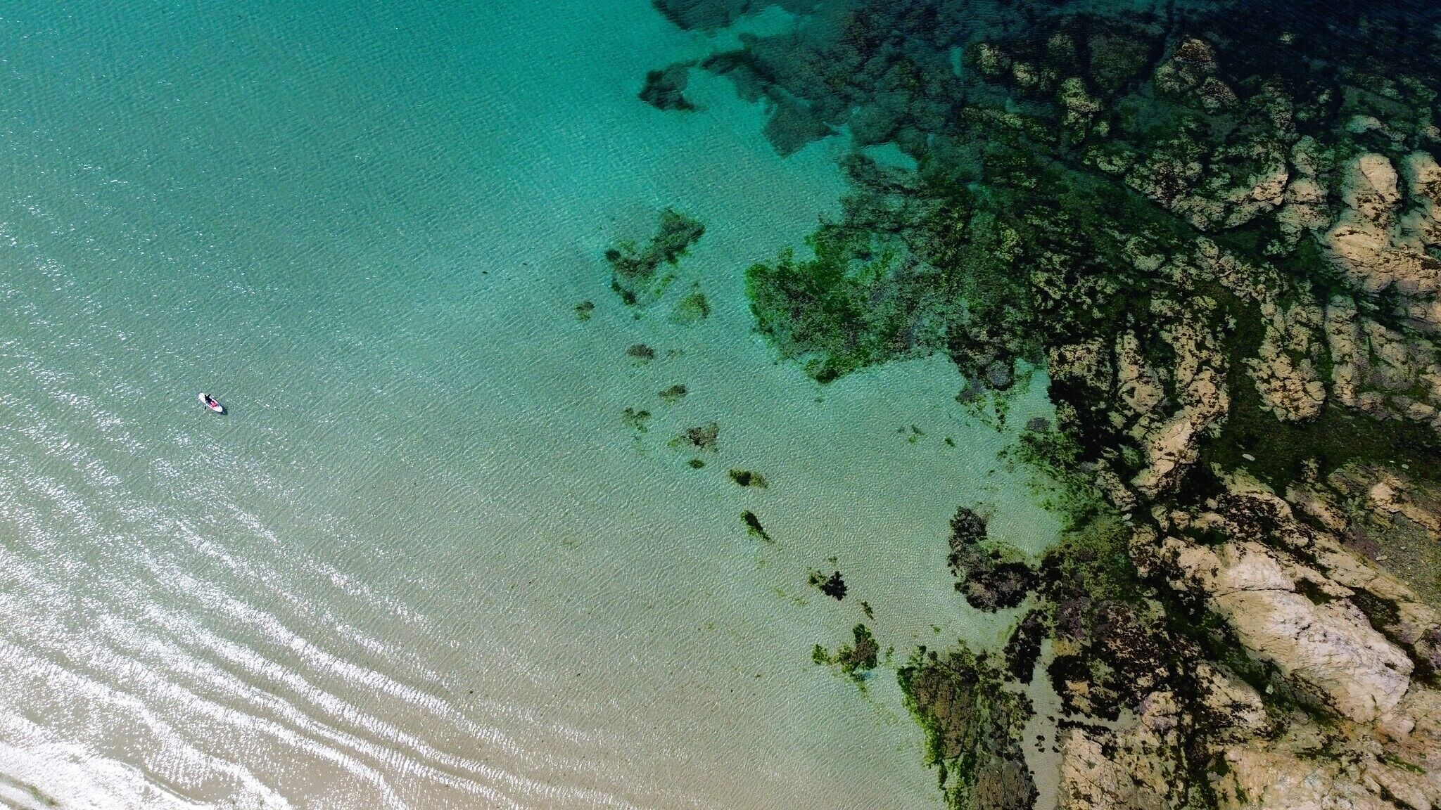 An aerial view of a coastal area with clear water, rocky outcrops, and a small boat.