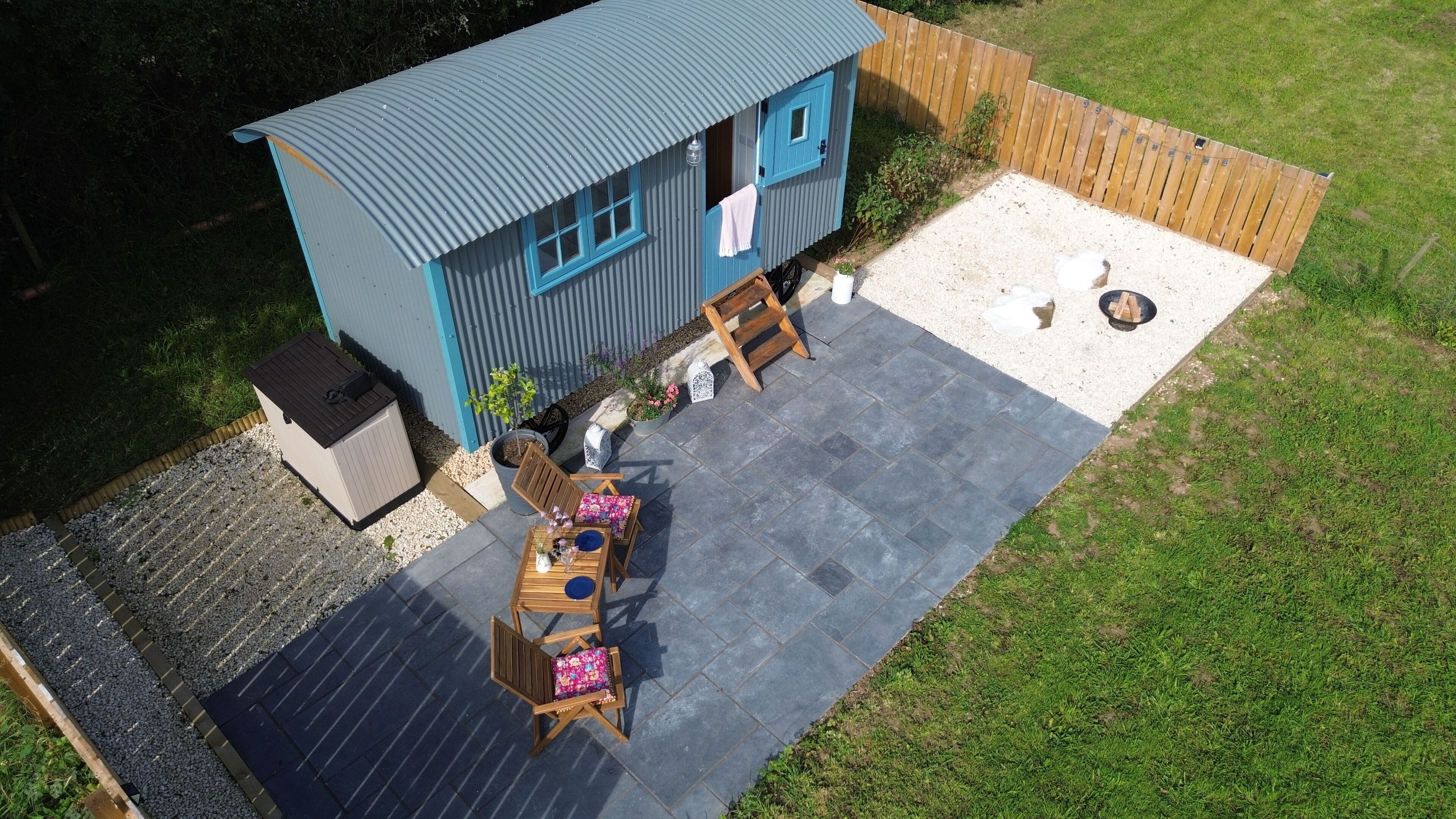 Una casa pequeña azul con un patio, una mesa de madera con sillas y un jardín pequeño.