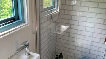 A modern bathroom with a glass shower enclosure, a sink with a chrome faucet, and a window with blue curtains.