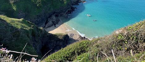 Un paysage côtier avec une plage, des falaises et une petite île au loin.