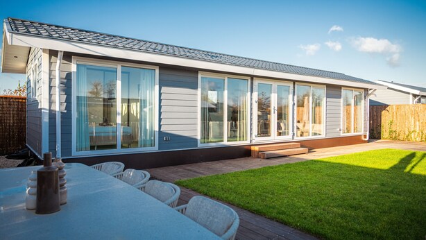 Una casa moderna con una terraza grande, un césped cuidado y un comedor con mobiliario de exterior.