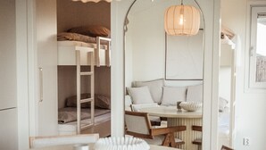 Una habitación moderna y compacta con una mesa redonda, sillas de madera, una litera y un espejo grande.