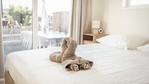 Una cama bien tendida con una toalla doblada al pie, una lámpara de noche y vistas al exterior a través de un ventanal amplio.