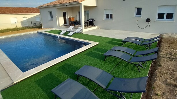 A swimming pool with artificial grass and lounge chairs, a covered patio, and a building with a tiled roof. - Villa with 4 bedrooms and pool (FRESPECH)