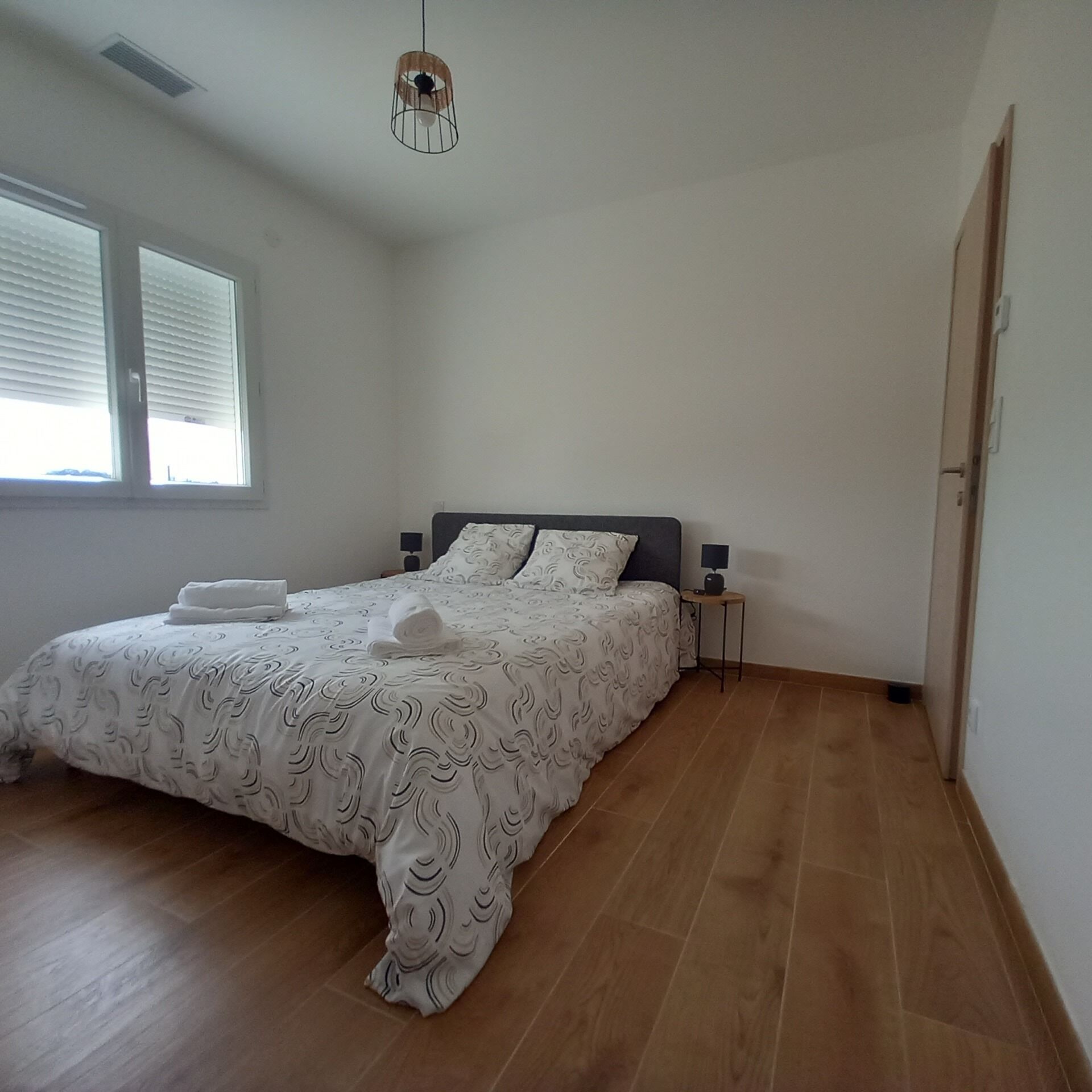 A bedroom with a bed, a bedside table, a lamp, and a window.