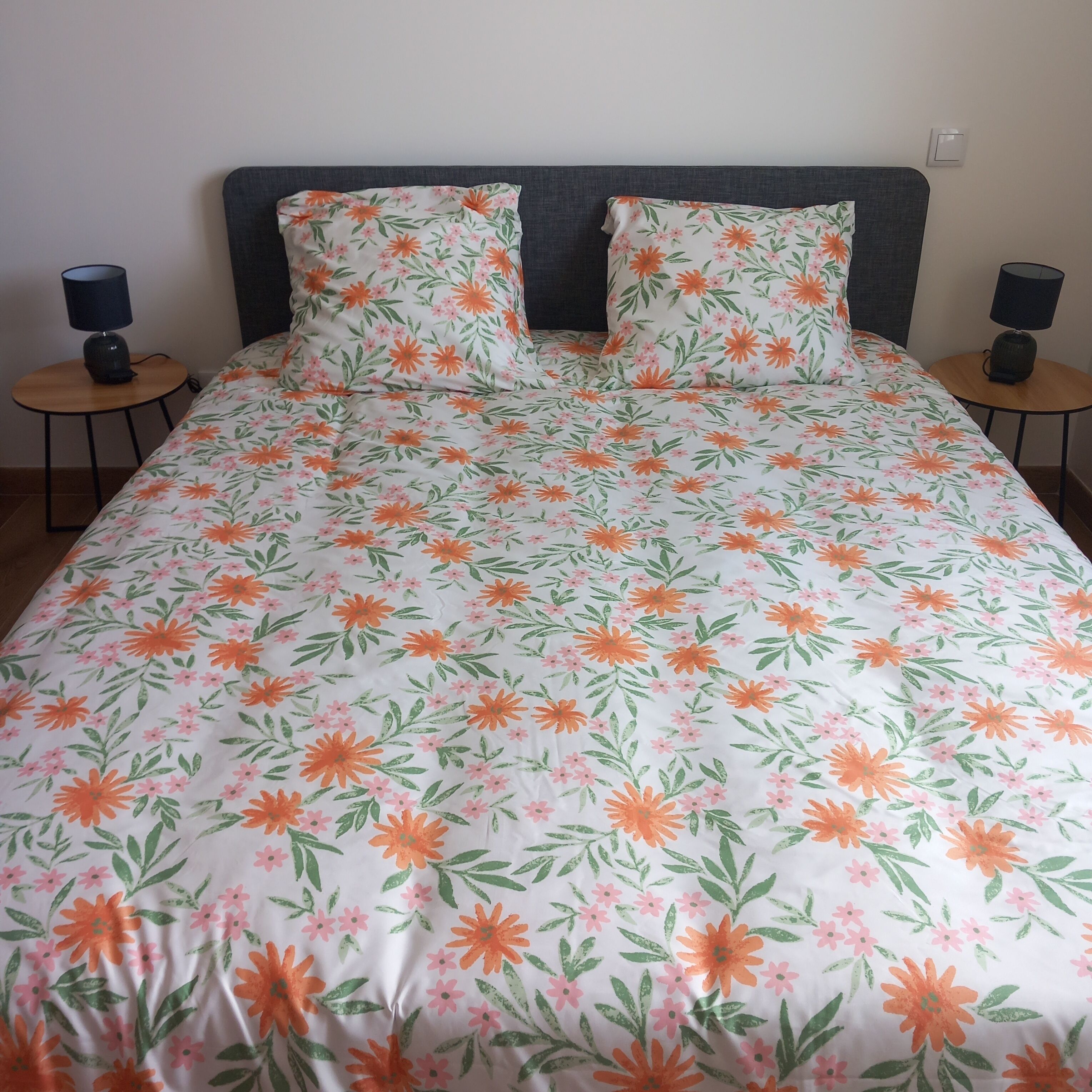 Un letto con copriletto floreale, due cuscini e due comodini con lampade.