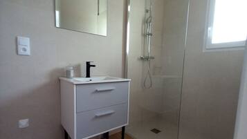 A bathroom with a white vanity, a mirror, a shower with a glass door, and a window providing natural light.