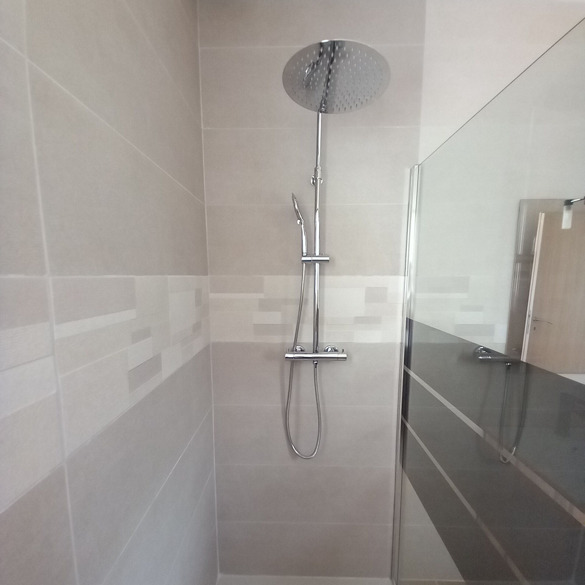 A modern shower with a rain shower head, handheld showerhead, and a handheld hose.