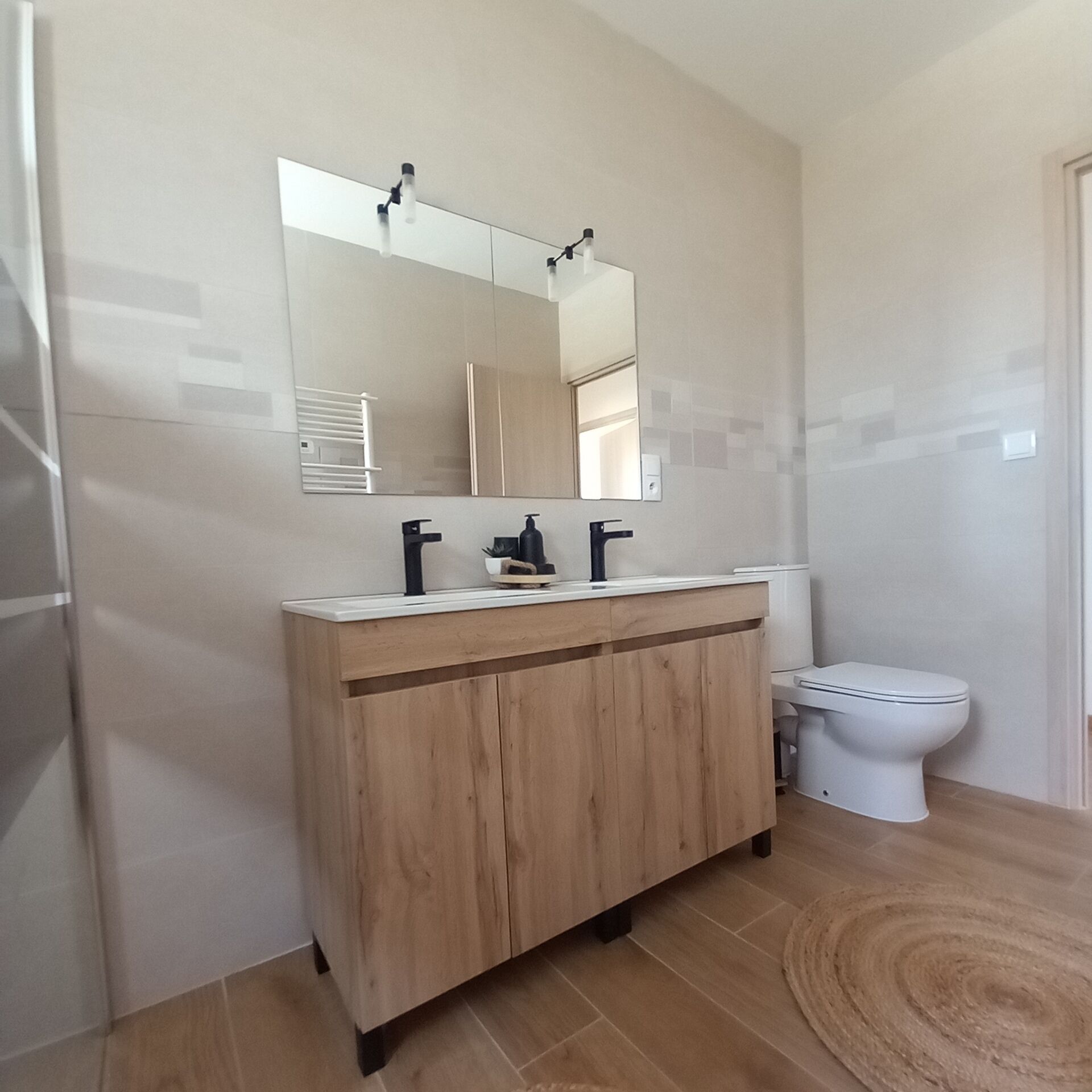 A modern bathroom with a wooden vanity, a mirror, a toilet, and a shower area.