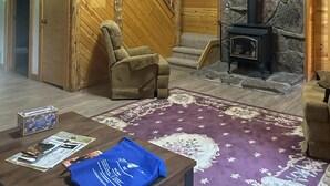 Un interior de madera con una escalera, una chimenea de piedra, un sofá y una mesa con revistas y una bolsa azul.