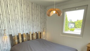 Een slaapkamer met een groot bed, een houten hoofdbord, een raam met uitzicht en een hangende lamp.