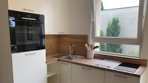 Een moderne keuken met witte kasten, een zwarte oven, een roestvrijstalen spoelbak en een raam met uitzicht op groen.