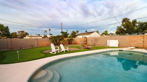 A swimming pool with a curved edge, surrounded by a brick wall and a grassy area with two white lawn chairs. - Beautiful home with backyard oasis!  Great Location for Spring Training trips! (Phoenix)