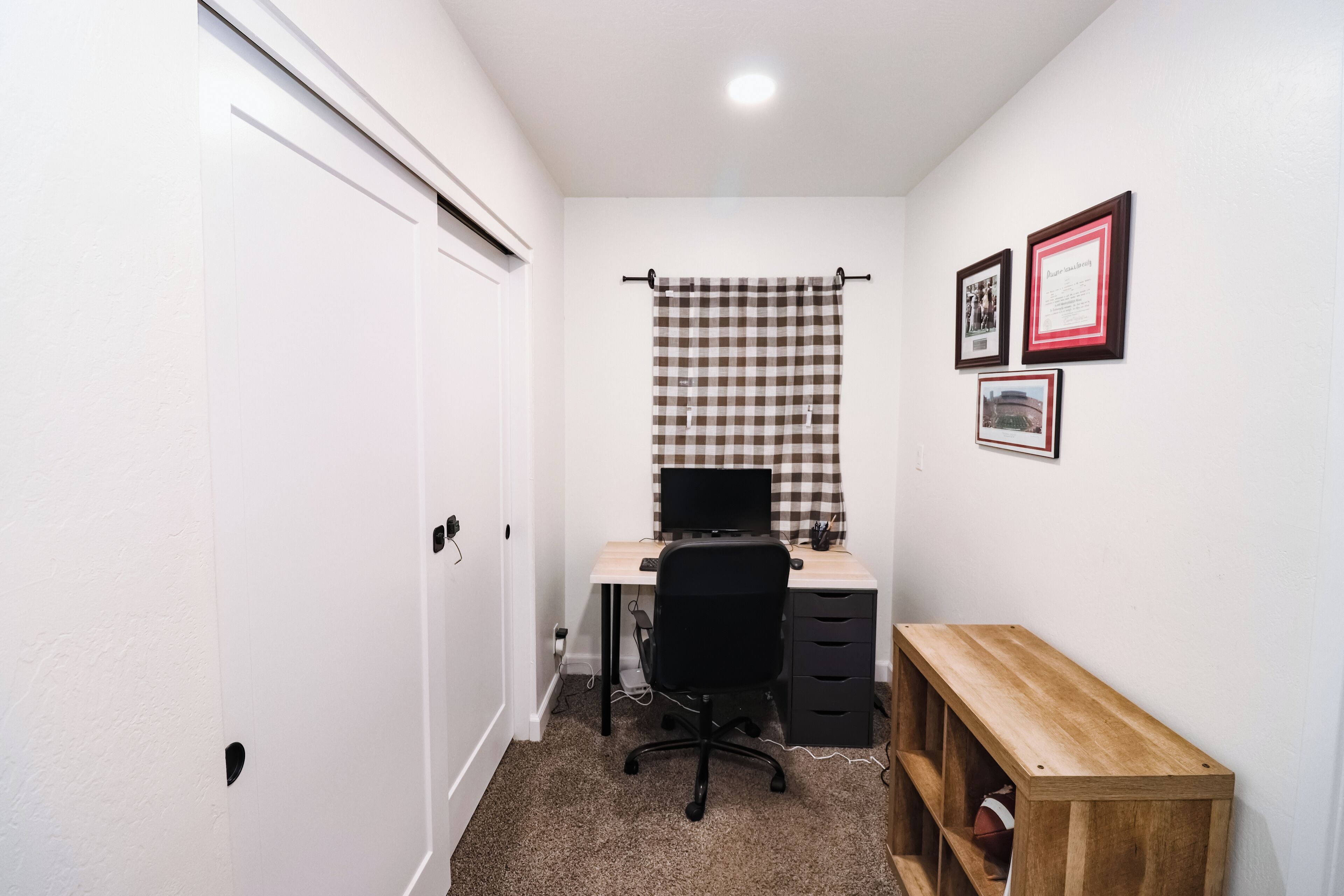 Een kleine, schone kamer met een bureau, stoel en een houten bankje.