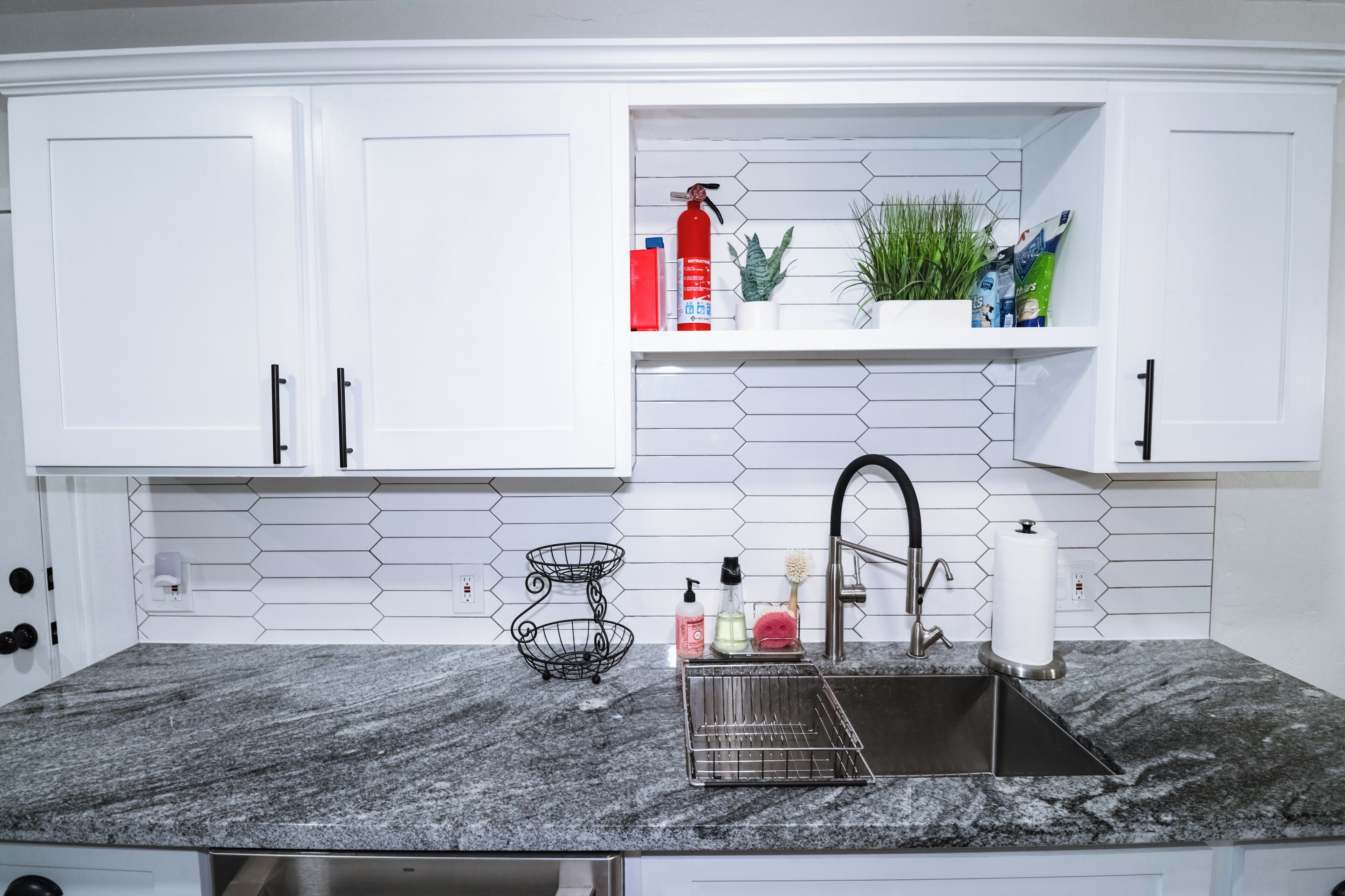 A kitchen with white cabinets, a granite countertop, a stainless steel sink, and a hexagonal tile backsplash.