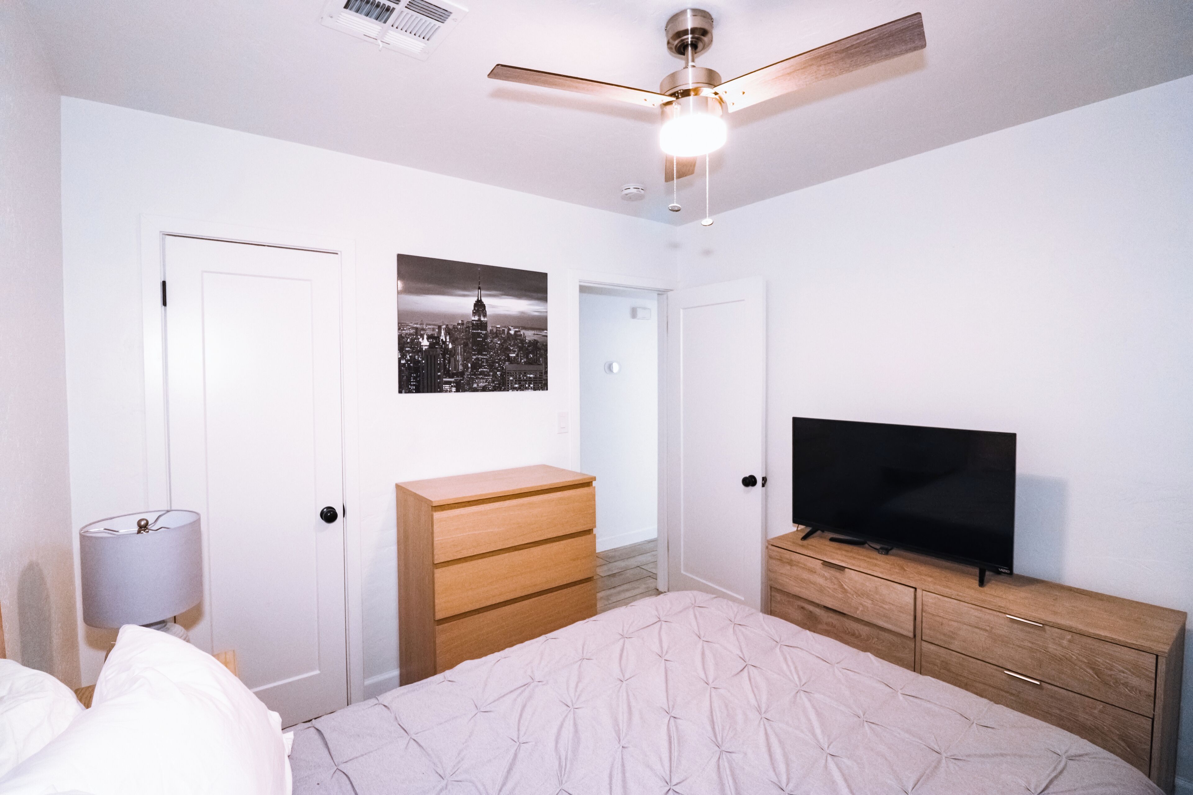 Un dormitorio con cama, cómoda, televisor y ventilador de techo.