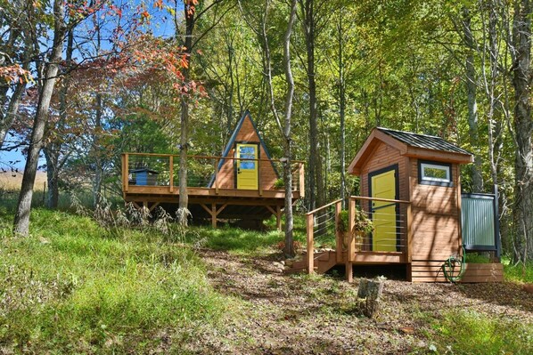 Eine Holzhütte mit einer Holzterrasse und einem kleinen Anbau, umgeben von Bäumen und einer natürlichen Landschaft.