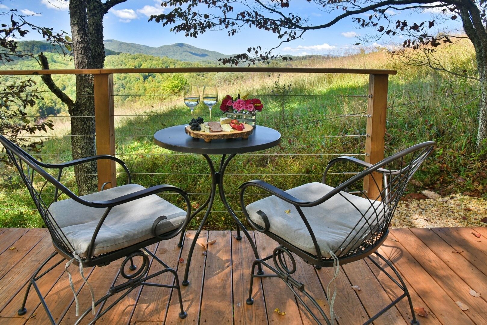 A wooden deck with two metal chairs and a table set for a meal.