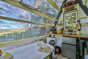 Eine gemütliche, kleine Küche mit Essecke, einem Bett und Blick durch ein von Regen benetztes Fenster.