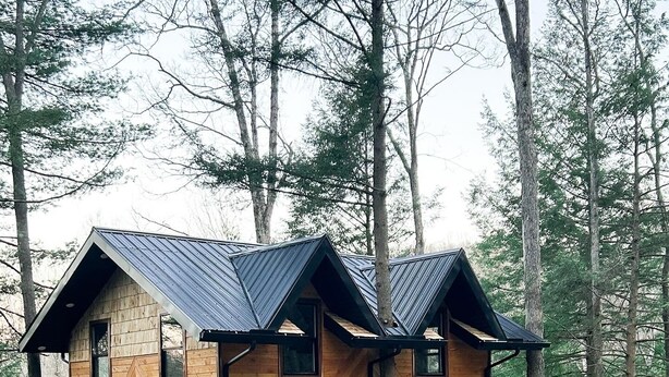 A wooden cabin with a hipped roof, a deck, and a staircase leading to the entrance.
