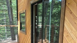 A wooden deck with glass doors leading to a forested area.