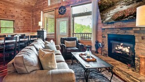 A cozy living room with a fireplace, leather sofa, and a stone fireplace surround. - Mountain Views, Hot Tub, Pool Table, Fire Pit, Dogs Welcome, 3 King Beds (Sevierville)