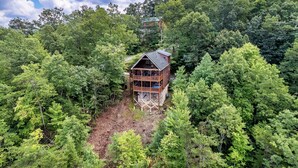 A wooden cabin surrounded by dense forest. - Mountain Views, Hot Tub, Pool Table, Fire Pit, Dogs Welcome, 3 King Beds (Sevierville)