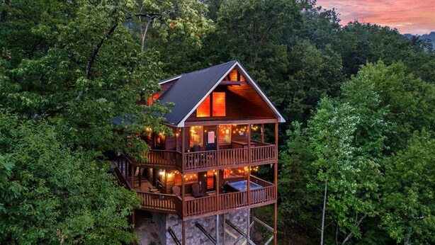 A wooden cabin with a balcony, surrounded by dense forest. - Mountain Views, Hot Tub, Pool Table, Fire Pit, Dogs Welcome, 3 King Beds (Sevierville)