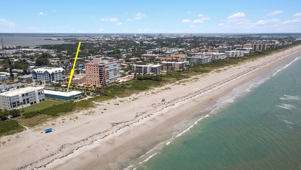 An aerial view of a coastal city with a wide beach, buildings, and a clear sky. - Oceanfront Paradise - Steps to Beach & Rocket Launches! (Cocoa Beach)