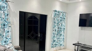 A modern living room with a grey sectional sofa, a flat-screen TV mounted on the wall, and a glass door leading to a balcony. - Beautiful Top Apartment in St. Elizabeth, Jamaica with an amazing Mountain View! (Junction)