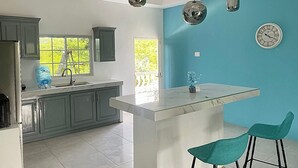 A modern kitchen with grey cabinets, a marble island, teal chairs, and pendant lights. - Beautiful Top Apartment in St. Elizabeth, Jamaica with an amazing Mountain View! (Junction)