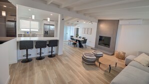 A modern kitchen with a bar area, a dining space with a table and chairs, and a living area with a sofa and ottomans.