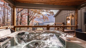 Ein Whirlpool mit einer Holterrasse und Blick auf Herbstbäume und Berge.