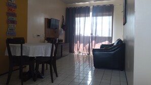 Ein Essbereich mit Tisch und Stühlen, einem Fernseher auf einem Standfuß, einem Ventilator und einer Couch.