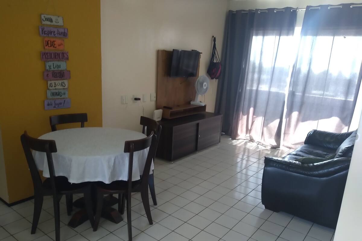 A dining area with a table and chairs, a sofa, a TV, and a fan.