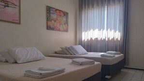 Ein Hotelzimmer mit zwei Betten, jeweils mit weißer Bettwäsche und Kissen, einem großen Fenster mit Vorhängen und einem Gemälde an der Wand.