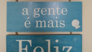 Ein Holzschild mit der Aufschrift 'Perto do Mar' und 'a gente é mais Feliz' im Küstenstil.