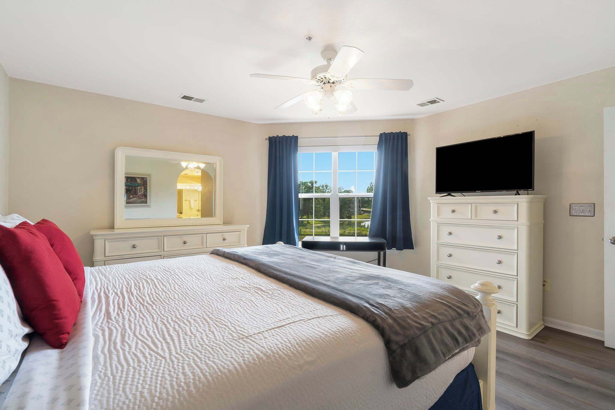 A bedroom with a bed, a dresser, a television, and a window with curtains.