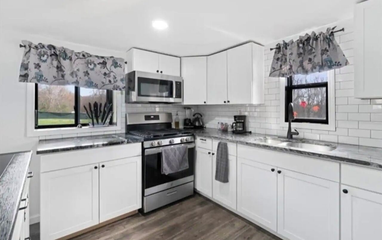 A modern kitchen with white cabinets, a stainless steel stove, a microwave, and a sink.