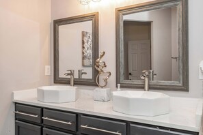 A bathroom with two sinks, a marble countertop, and a large mirror with a decorative metal piece. - Urban Escape (Cincinnati)