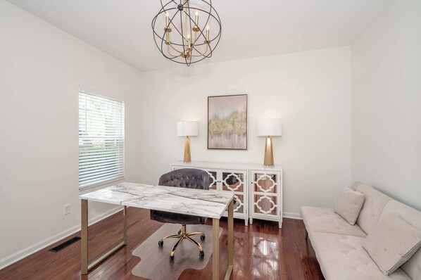 A room with a marble table, a grey upholstered chair, a white console with decorative panels, a beige sofa, and a chandelier. - Urban Escape (Cincinnati)