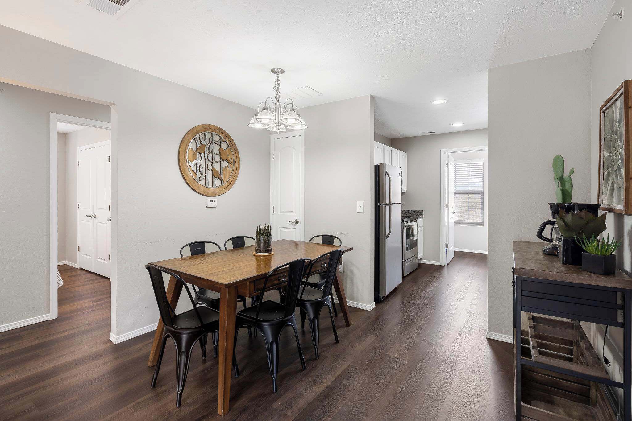 A modern kitchen with a dining area, featuring a wooden table, black chairs, and a chandelier.