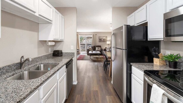 Cocina moderna con encimeras de granito, electrodomésticos de acero inoxidable y muebles de cocina blancos.