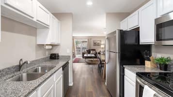 Cocina moderna con encimeras de granito, electrodomésticos de acero inoxidable y muebles de cocina blancos.